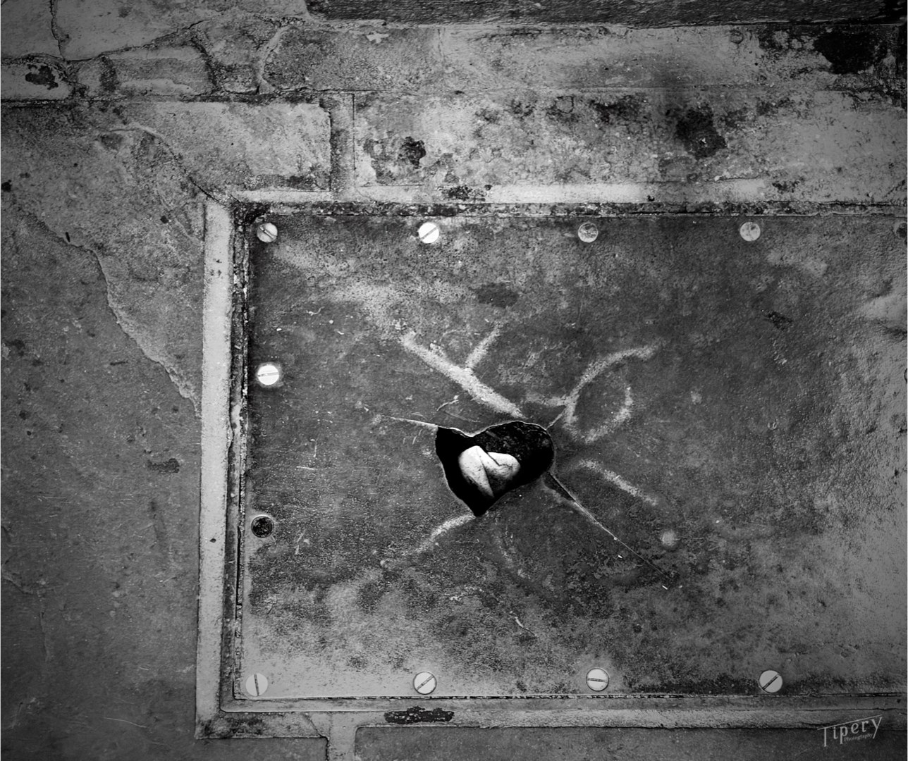 A square steel plate in the pavement, torn open in the shape of a heart
